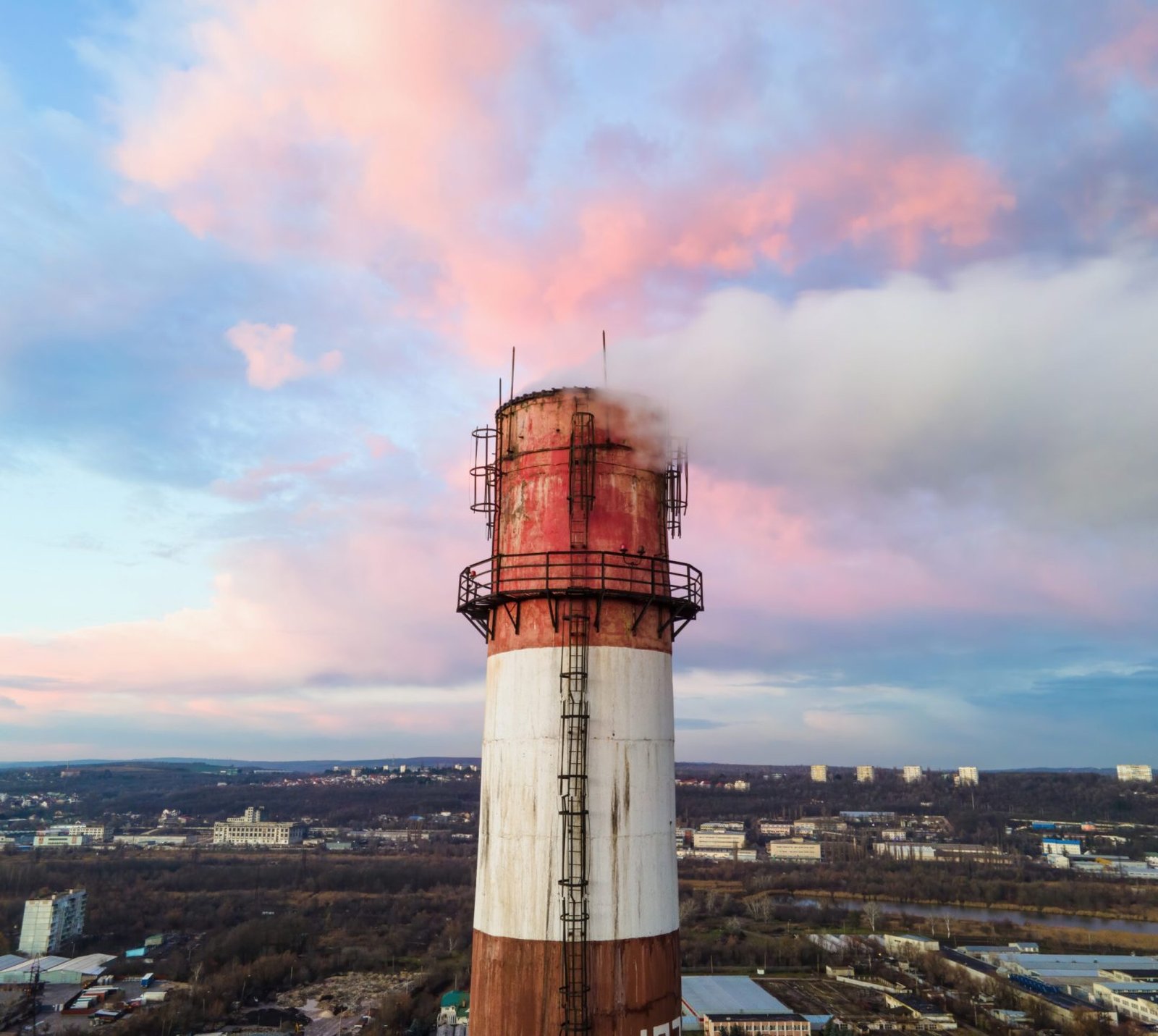 Aerial drone view of thermal station at sunset with smoke coming out of the tube. Buildings, trees and colored clouds on the background. Moldova